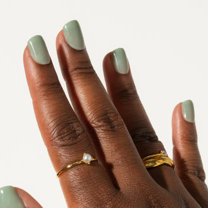 Close-up of a hand with green press on nails wearing two gold rings on a neutral background