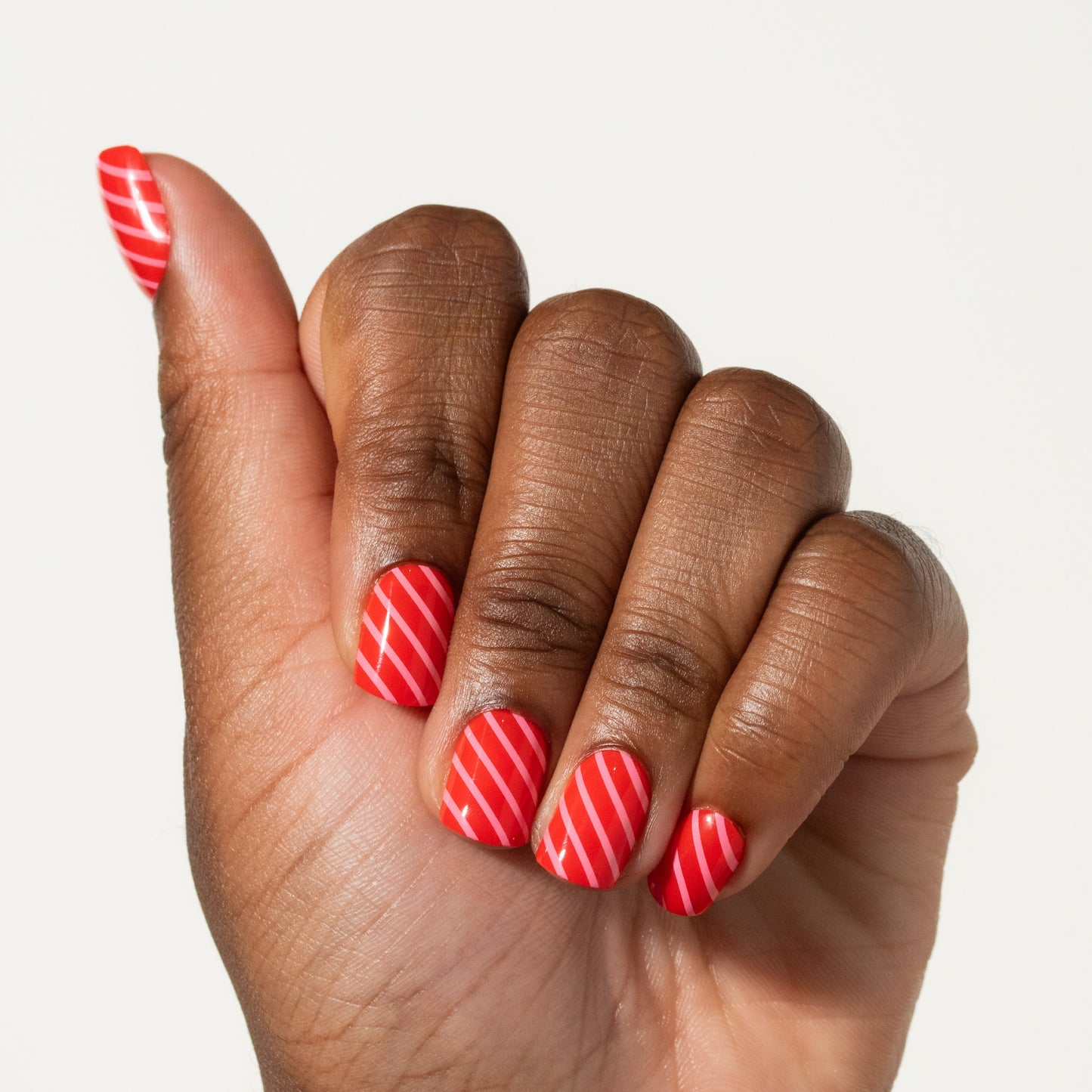 Hand with red and pink striped press on nails on a plain background