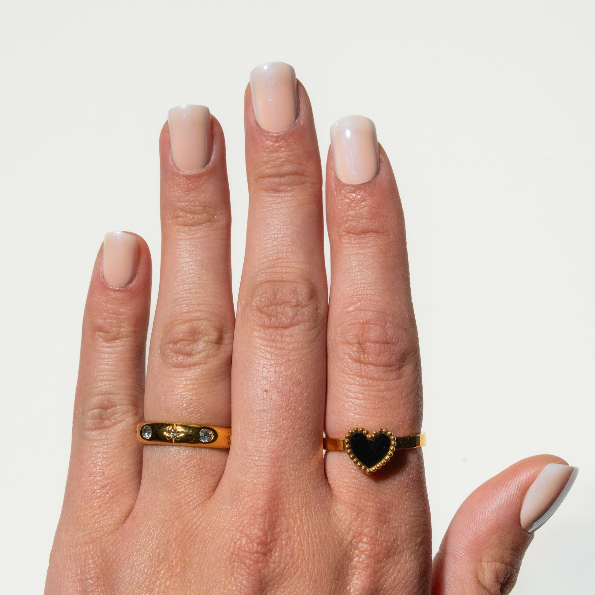 Hand wearing two gold rings with heart-shaped stones on a light background