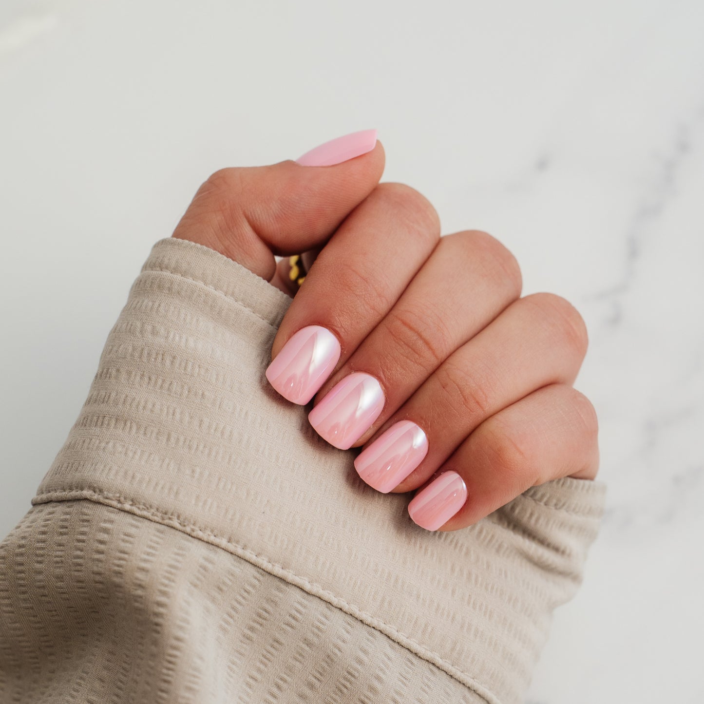 Hand with pink press on nails wearing a beige sleeve on a light background