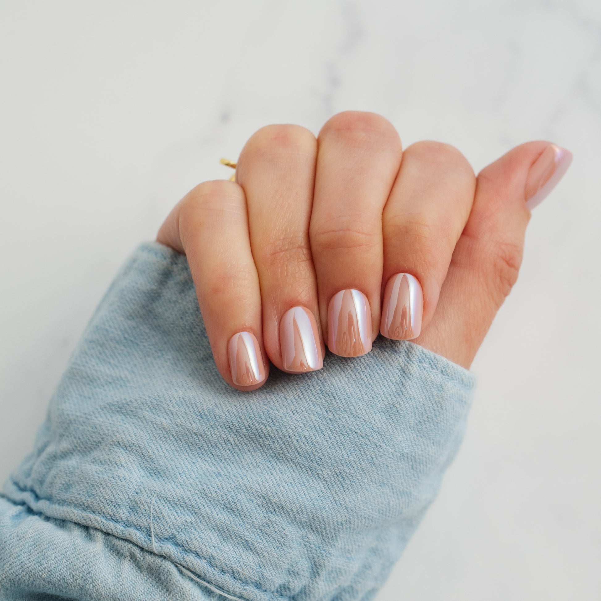Hand with light pink press on nails wearing a denim sleeve on a light background