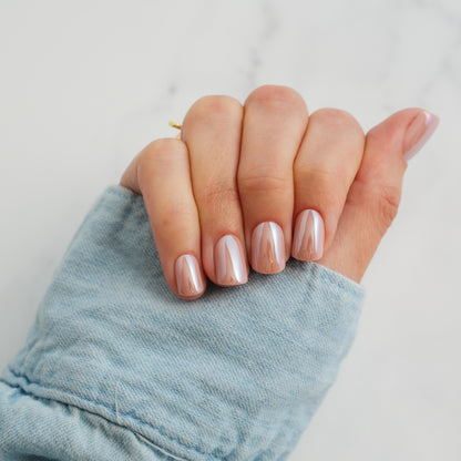Hand with light pink press on nails wearing a denim sleeve on a light background