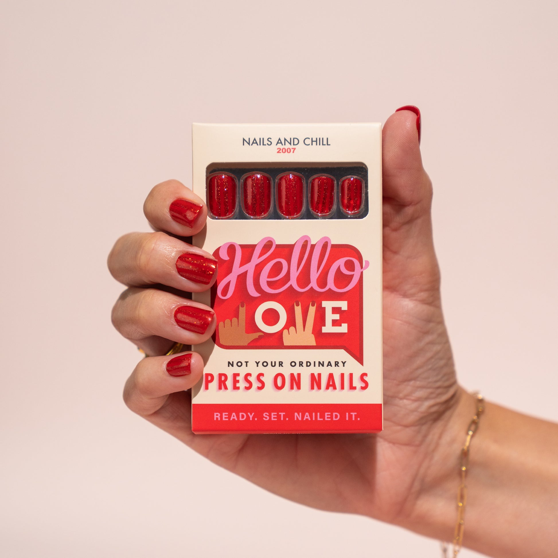 Hand holding a box of 'Hello Love' press-on nails with red nails.