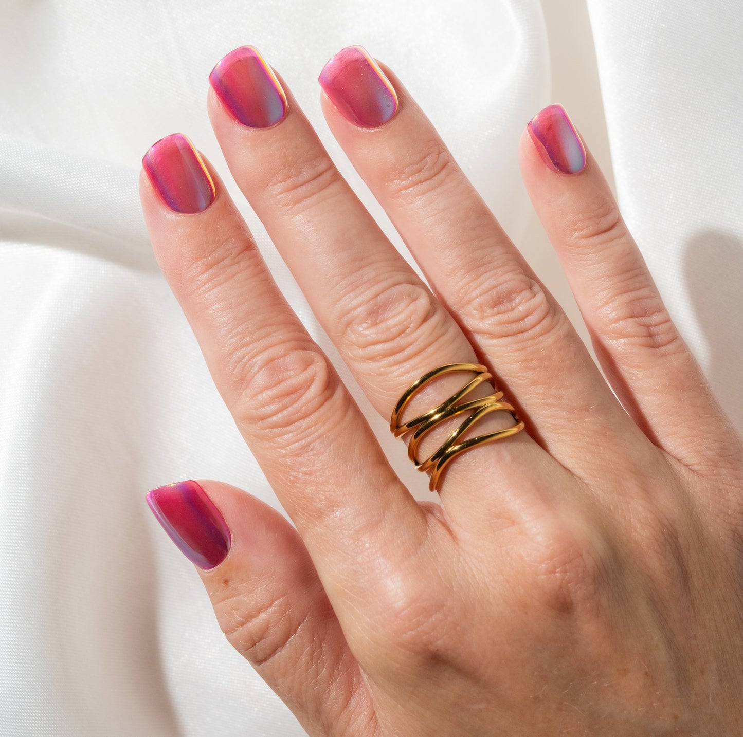 Hand with pink press on nails and gold rings on a white background