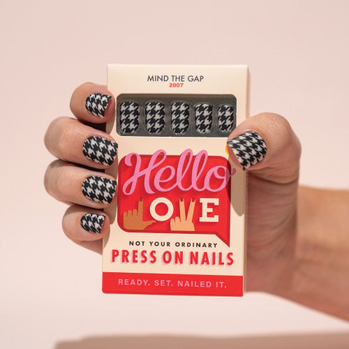 Hand holding a box of press-on nails with a 'Hello Love' design on a beige background