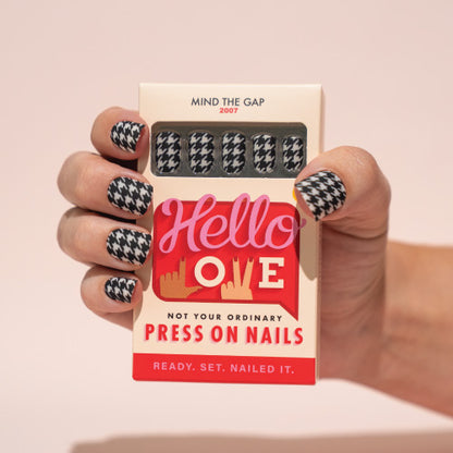 Hand holding a box of press-on nails with a 'Hello Love' design on a beige background