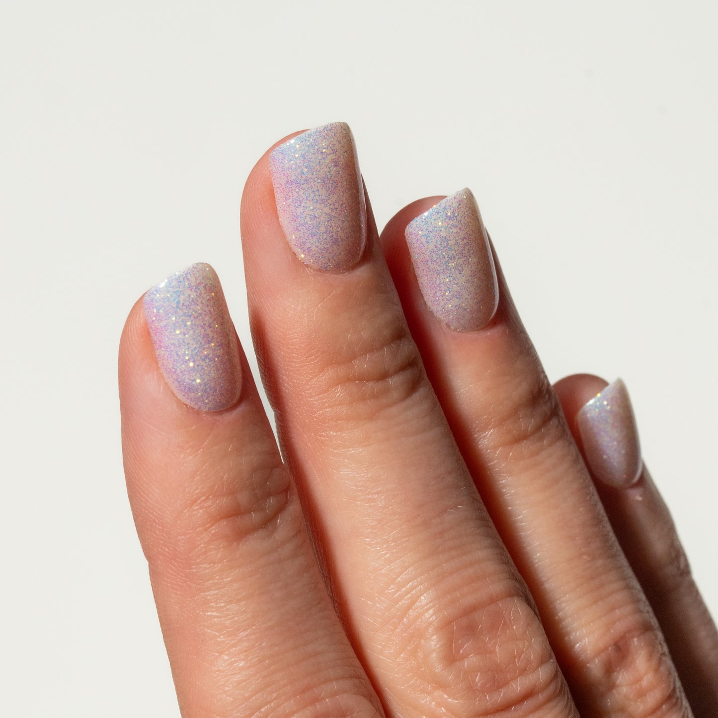 Hand with glittery pink press on nails on a light gray background