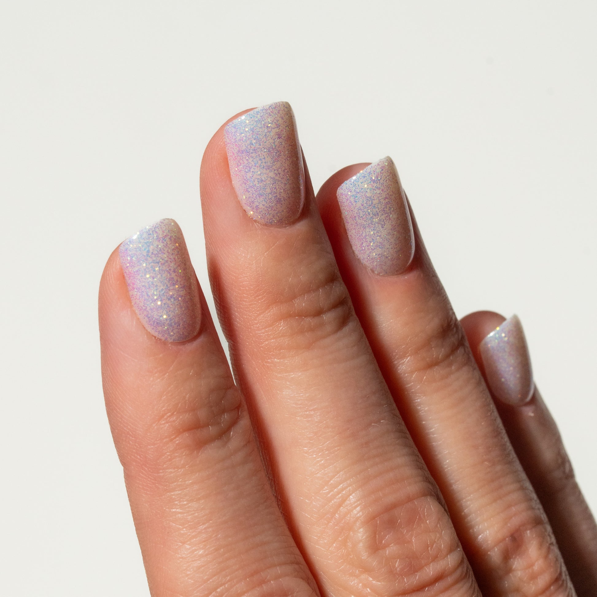 Hand with glittery pink press on nails on a light gray background