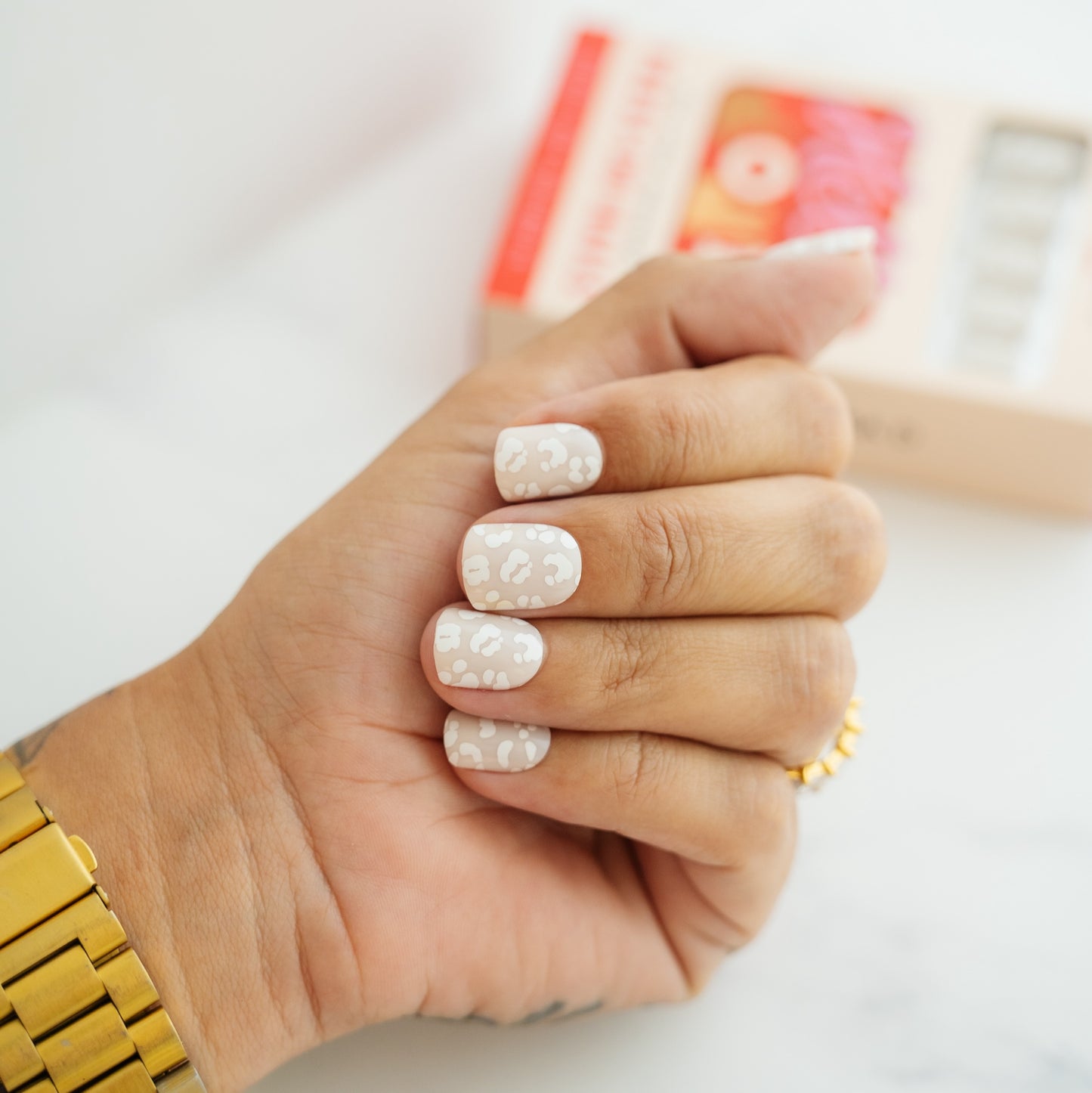 Hand with leopard press on nails wearing a gold watch and ring