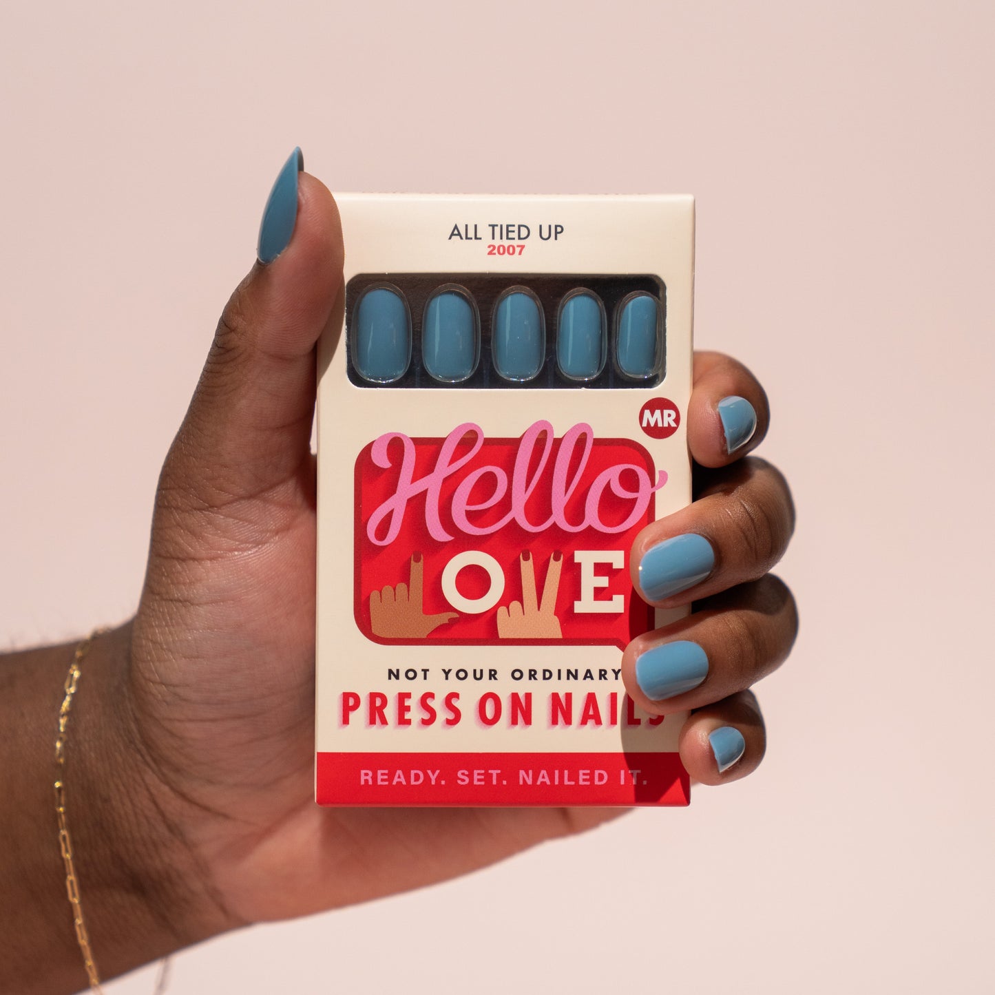 Hand holding a box of press-on nails with 'Hello Love' branding against a pink background