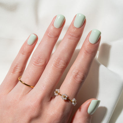 Hand with light green press on nails wearing two gold rings on a white background