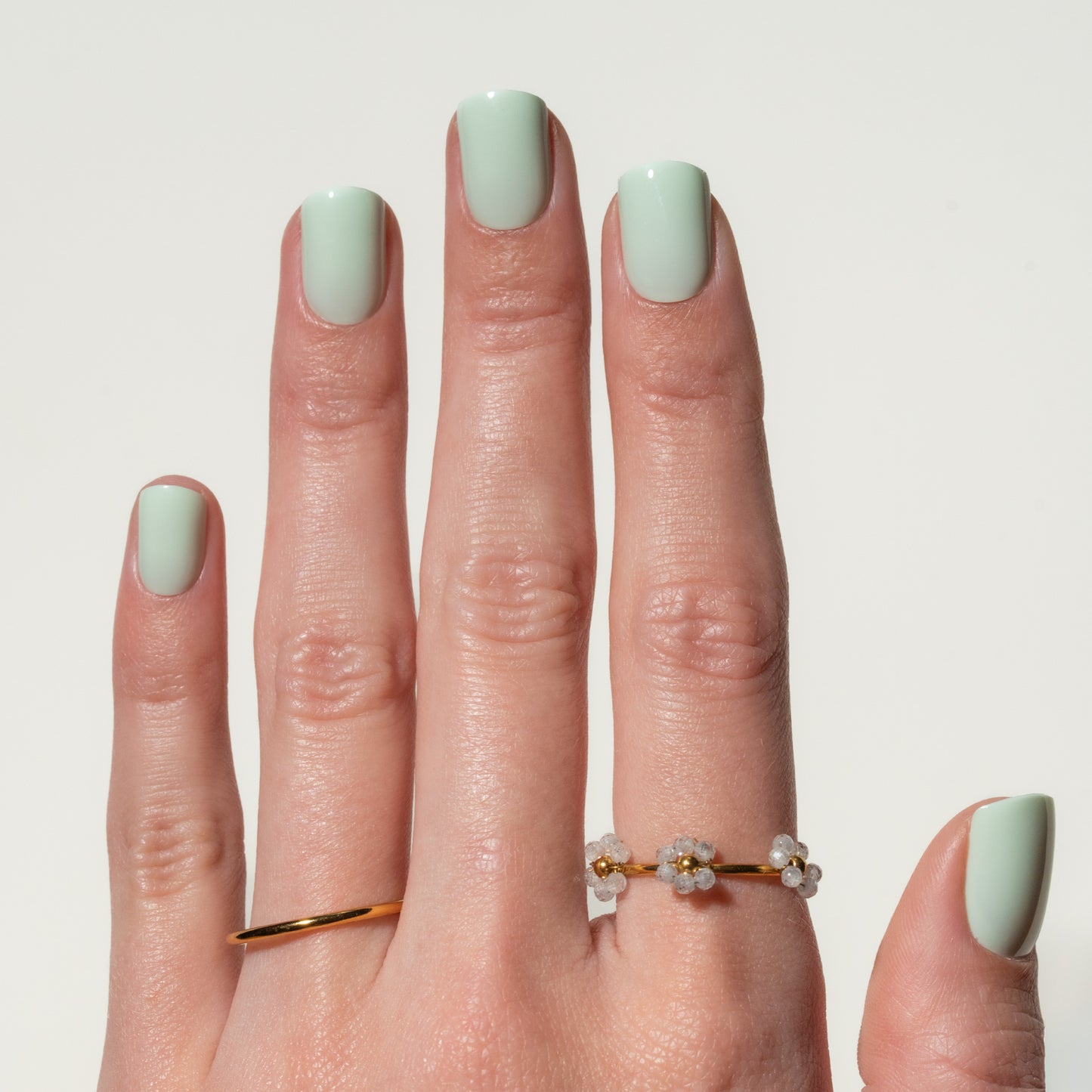 Hand with light green press on nails wearing a gold ring on a plain background