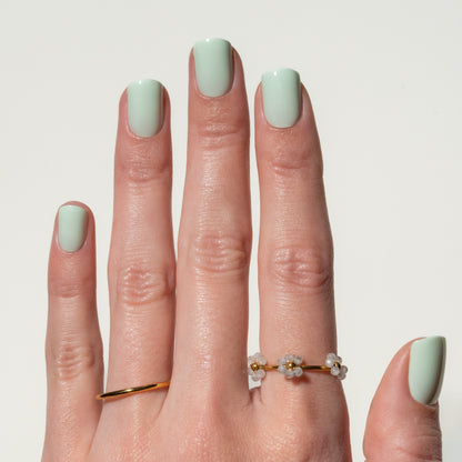 Hand with light green press on nails wearing a gold ring on a plain background