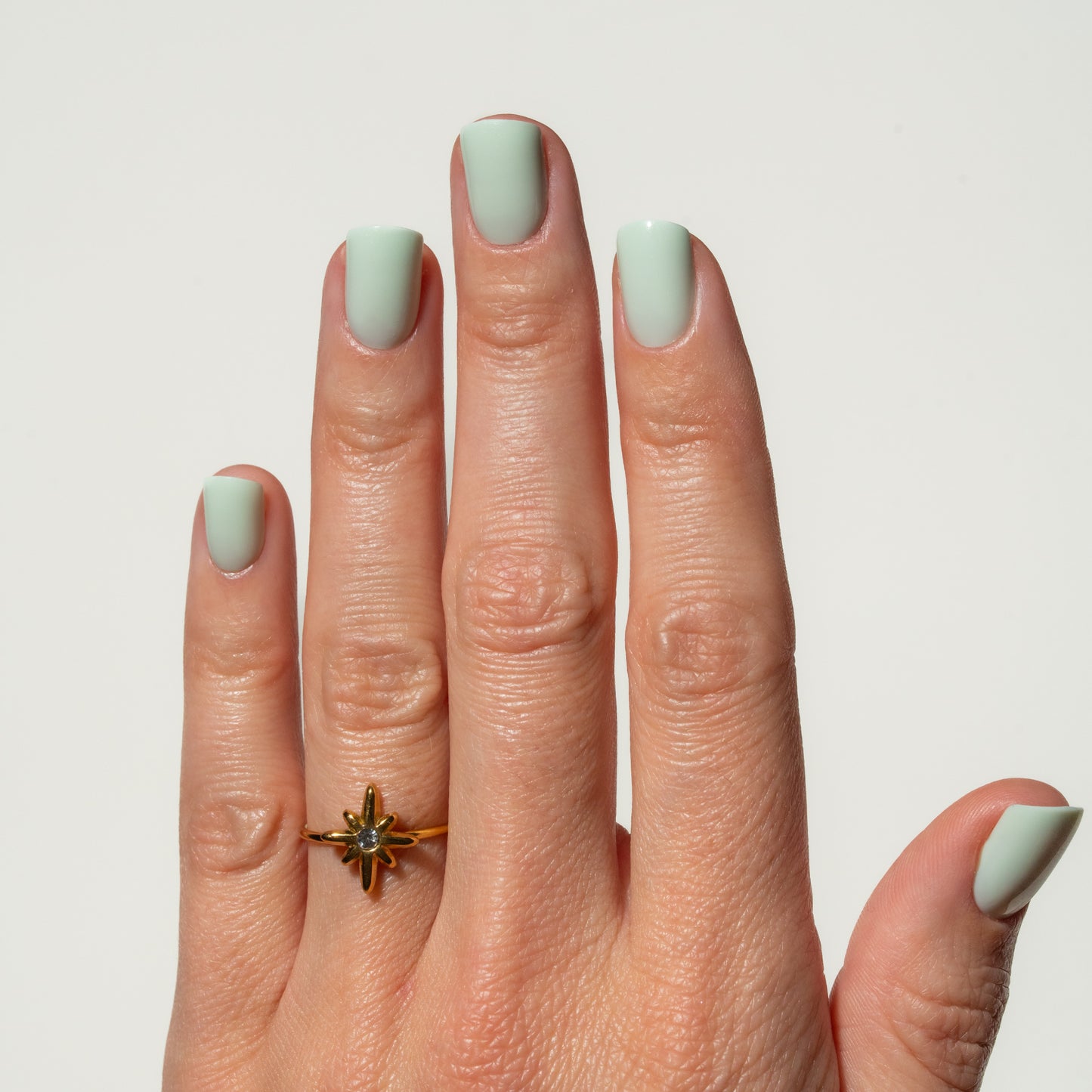 Hand with mint green nails wearing a gold ring on a light gray background