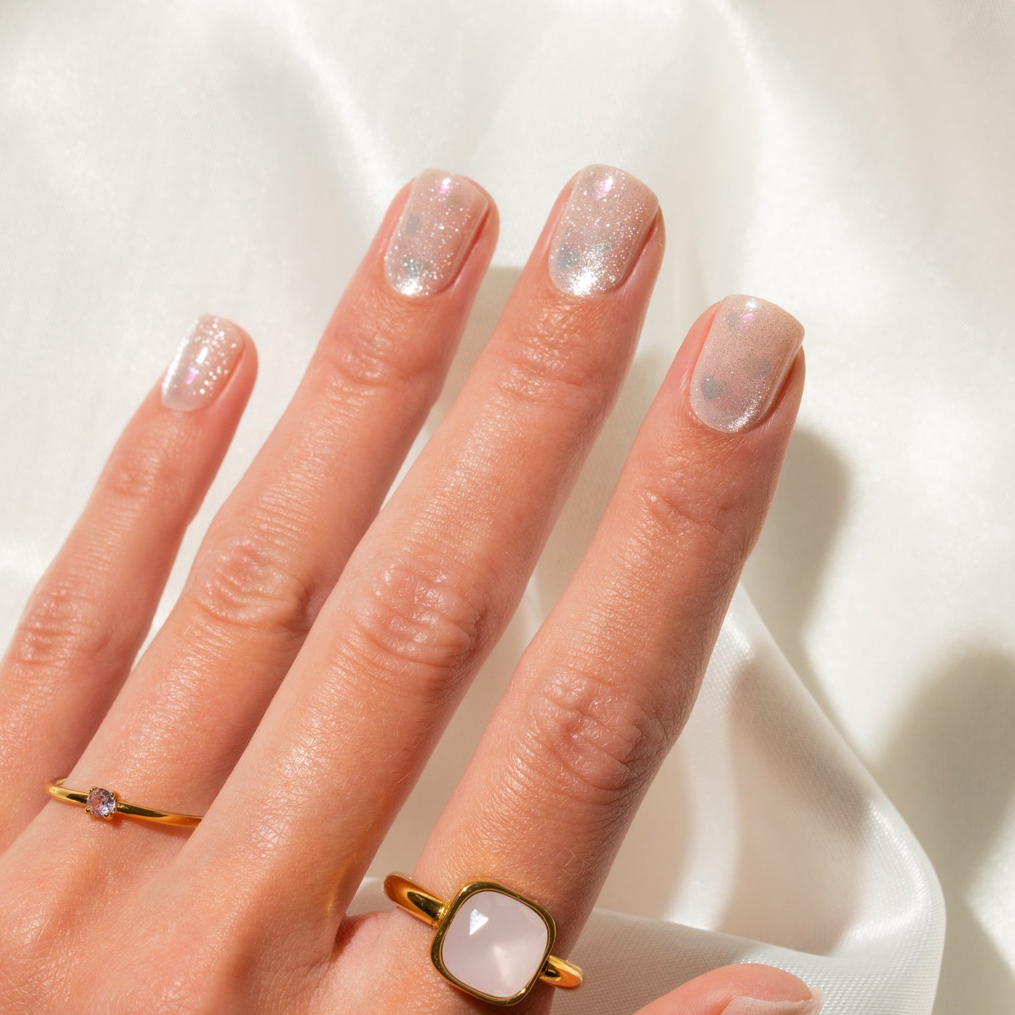 Hand with glittery press on nails and gold rings on a white background