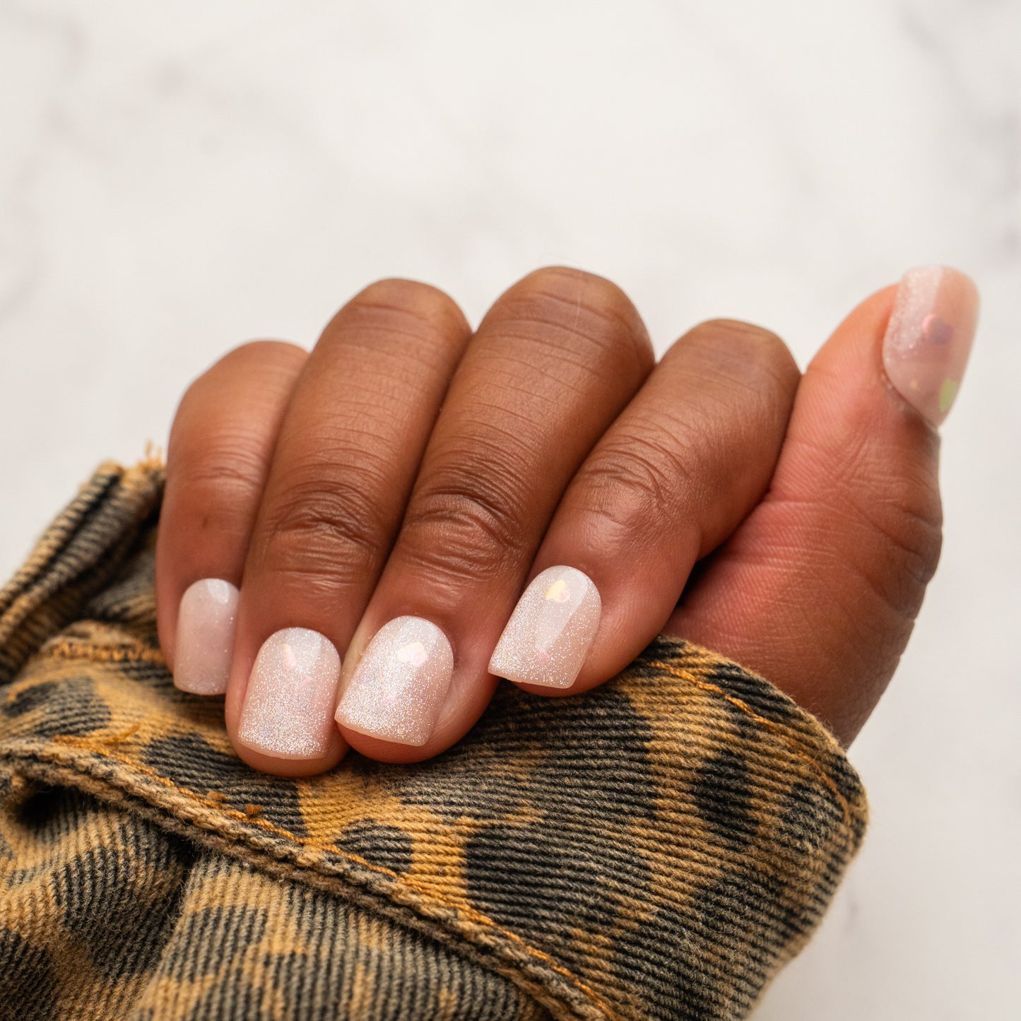 Close-up of a hand with light pink press on nails wearing a leopard print sleeve.