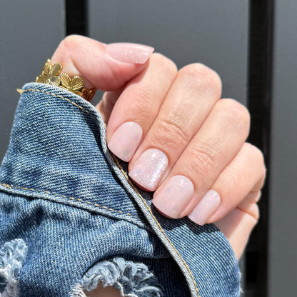 Close-up of a hand with pink press on nails wearing a gold ring, holding denim fabric.