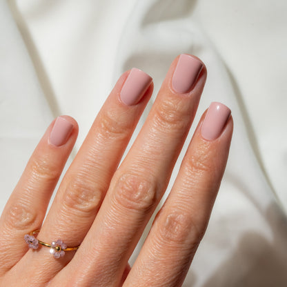 Hand with pink press on nails and a gold ring on a light background