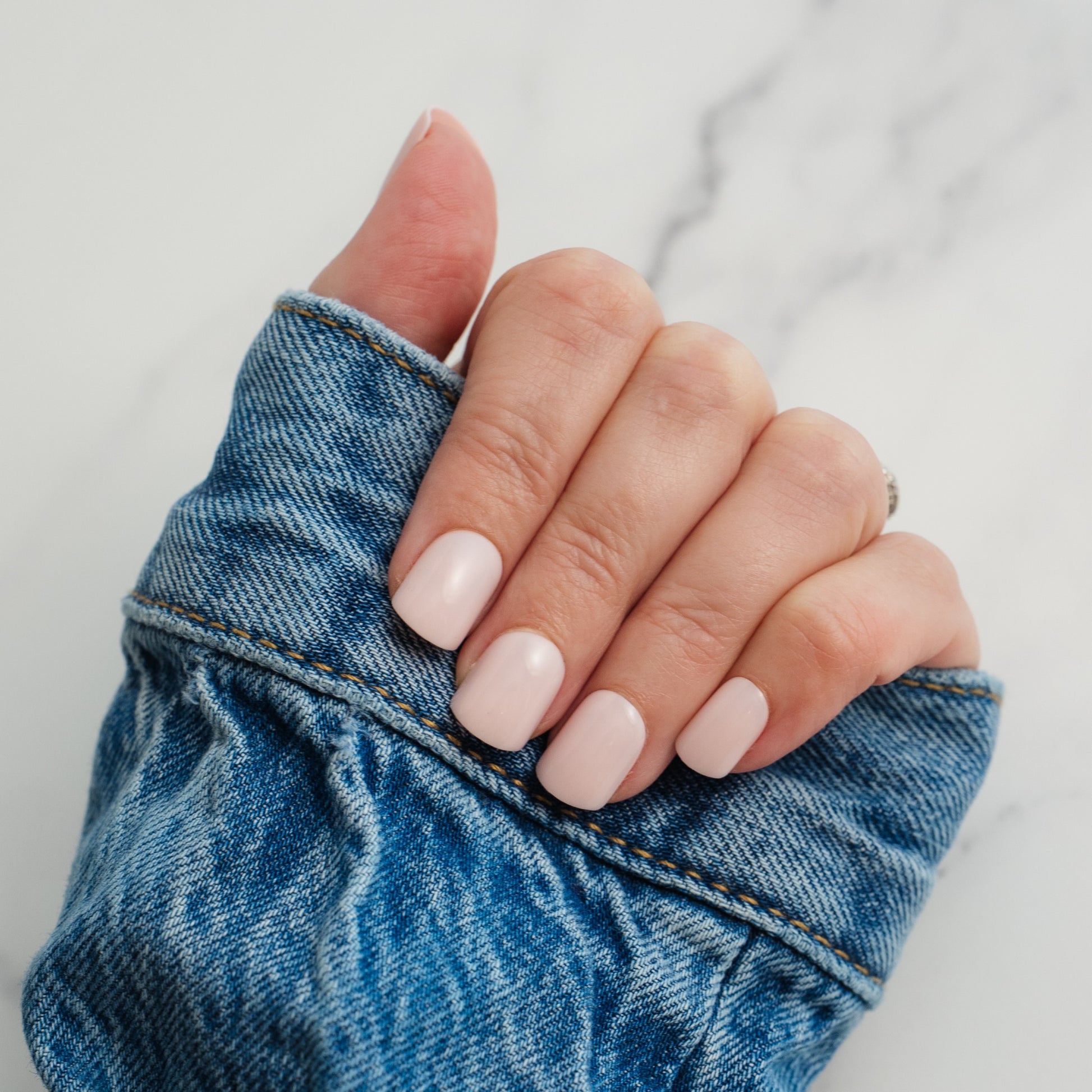 Hand with light pink press on nails holding a blue denim fabric