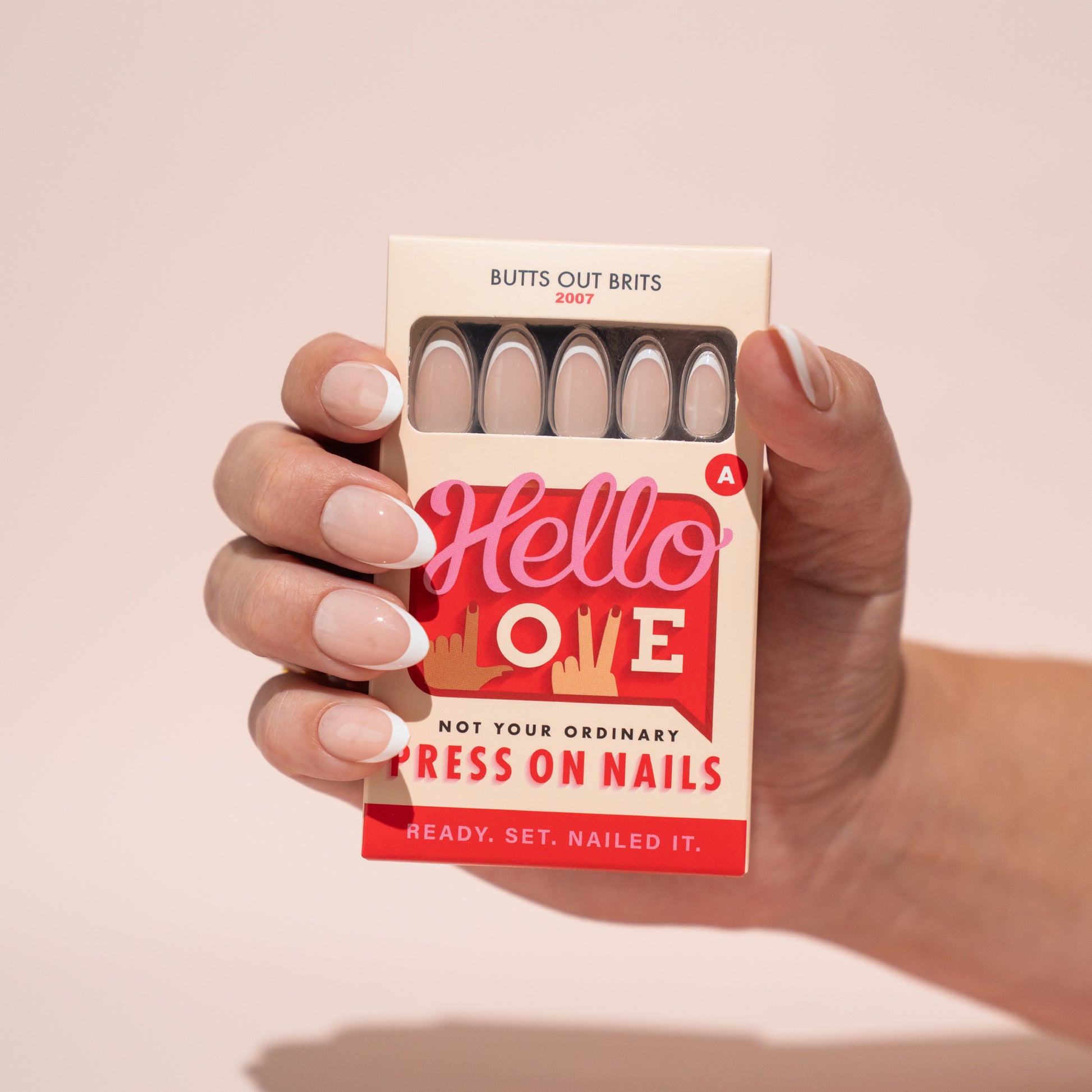 Hand holding a box of press-on nails with 'Hello Love' branding on a beige background