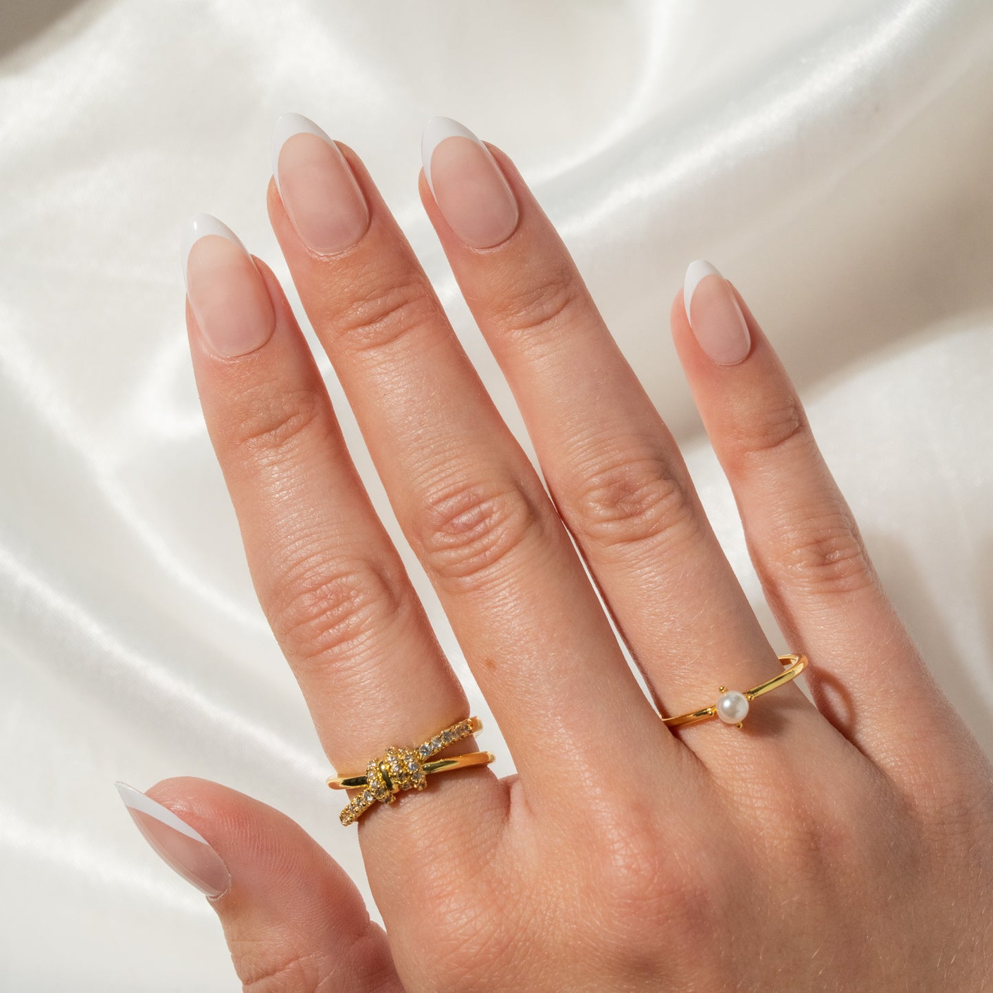 French manicured Hand wearing two gold rings with a pearl on a white background