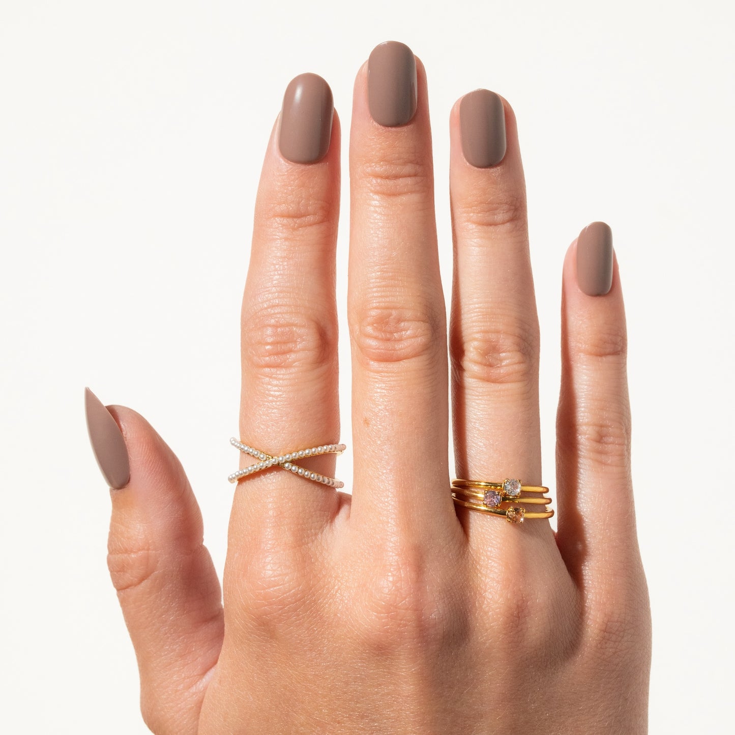 Hand wearing two gold rings with a plain background