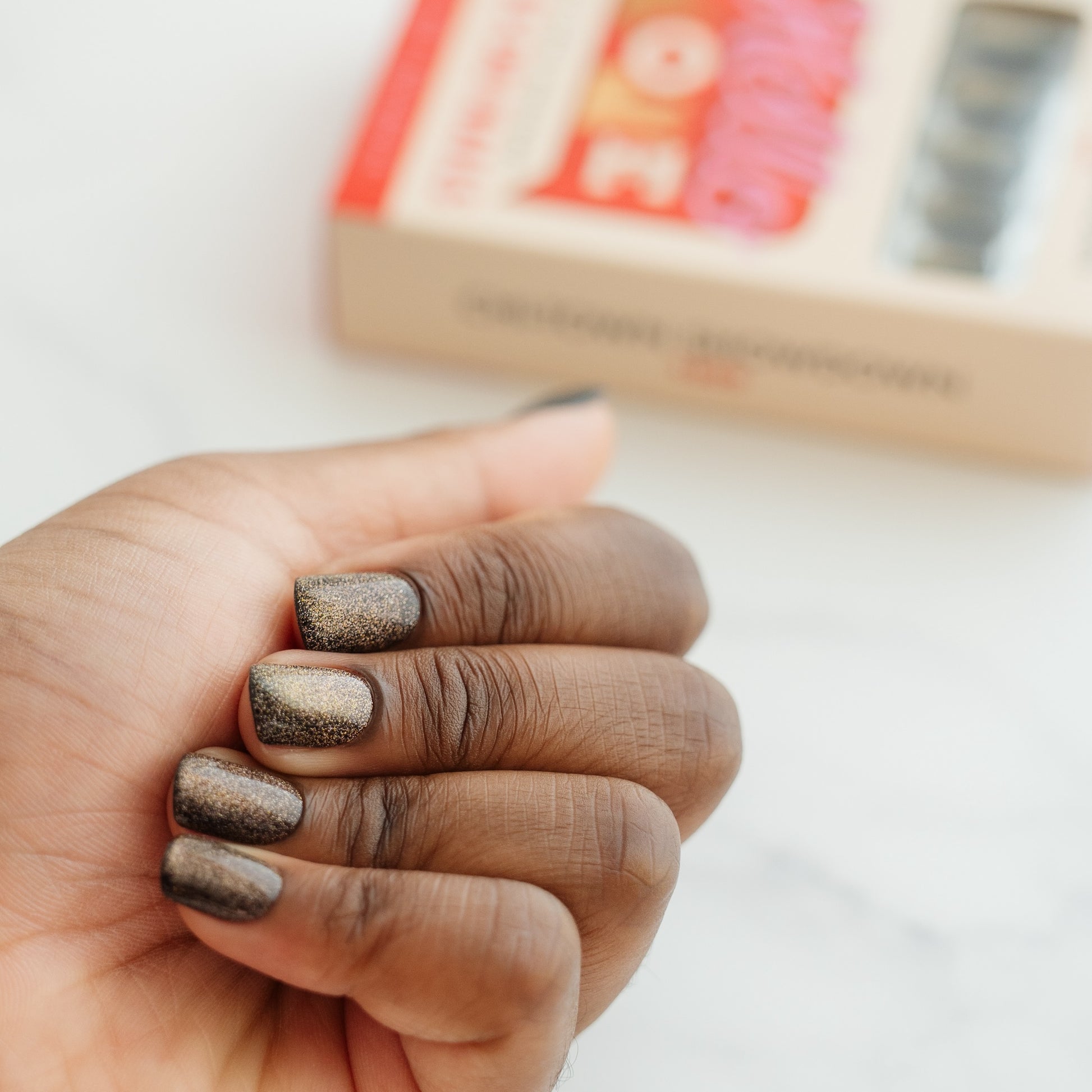 Hand with metallic press on nails holding a small object, with a blurred background