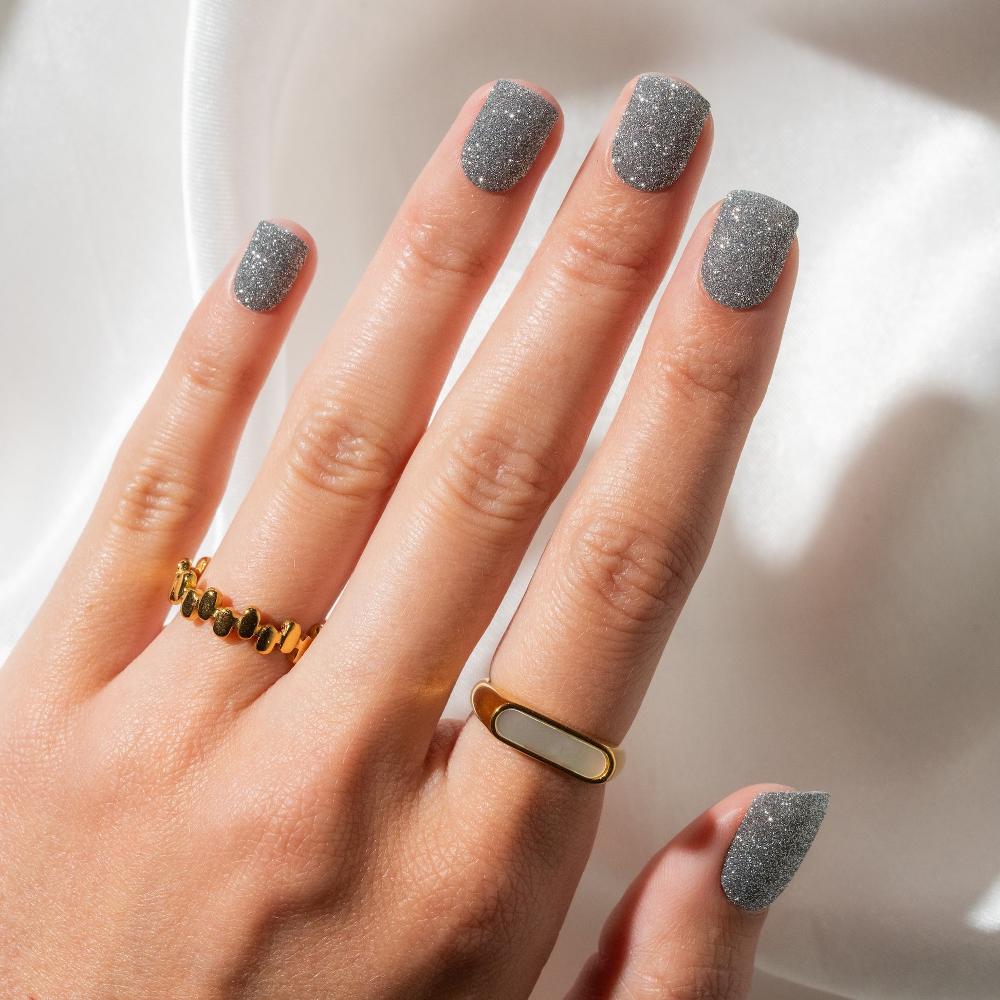 Hand with gold ring and glittery nails against a neutral background