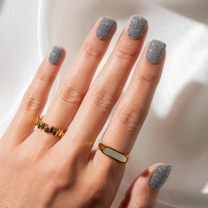 Hand with gold ring and glittery nails against a neutral background