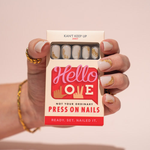 Hand holding a box of press-on nails with 'Hello Love' branding on a pink background