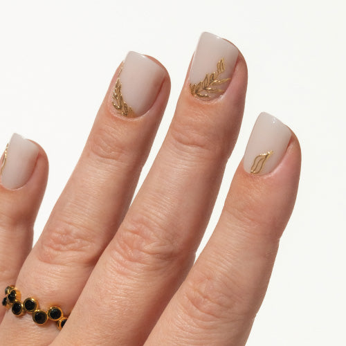 Hand with milky white press on nails and gold leaf designs on a white background KKU