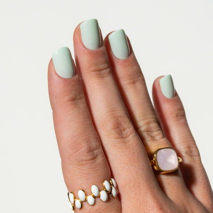 Hand with light green press on nails wearing gold rings on a plain background