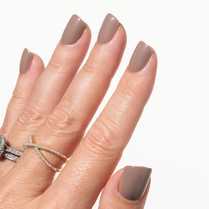 Hand with mocha brown press on nails wearing a gold ring on a white background