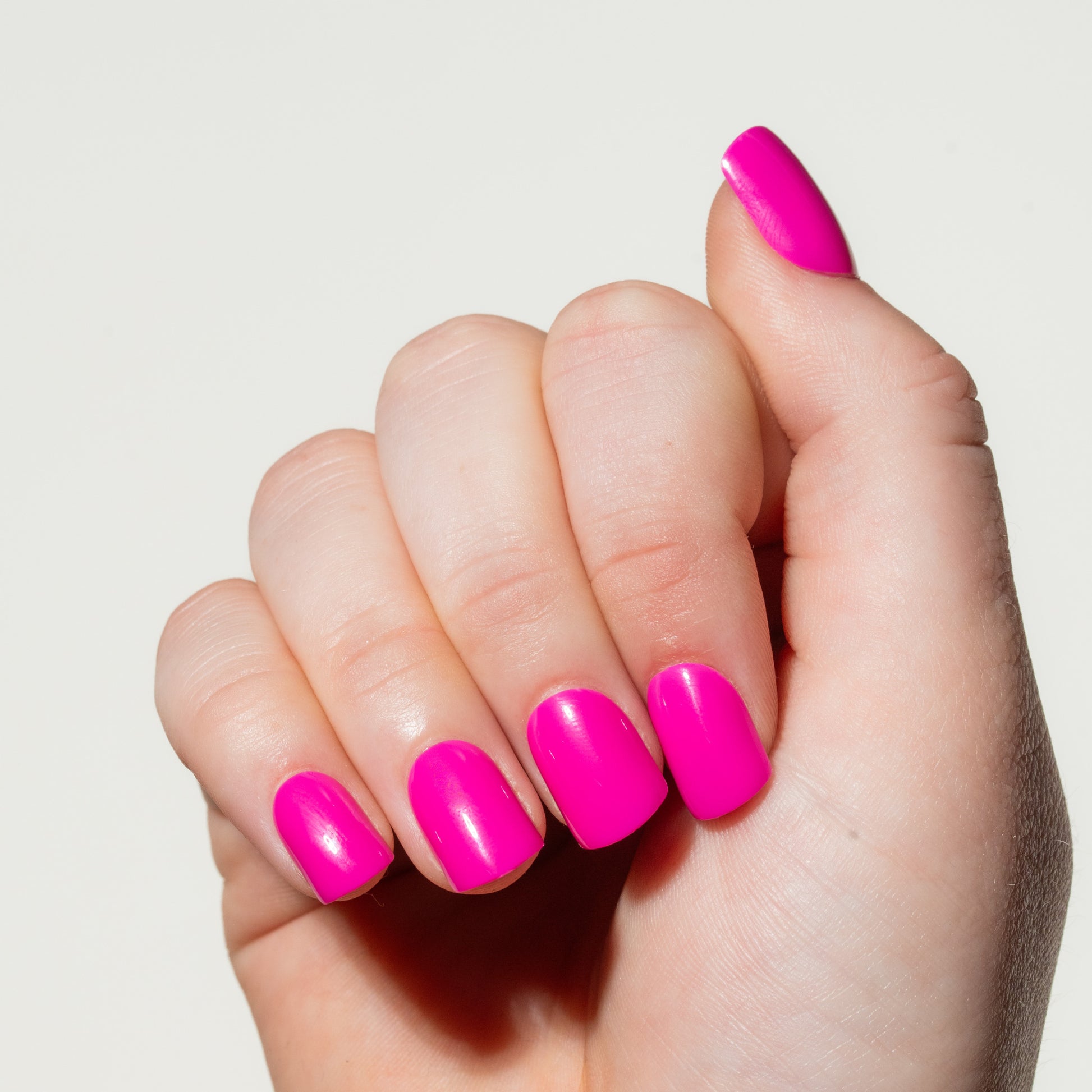 Hand with bright pink nails on a light background