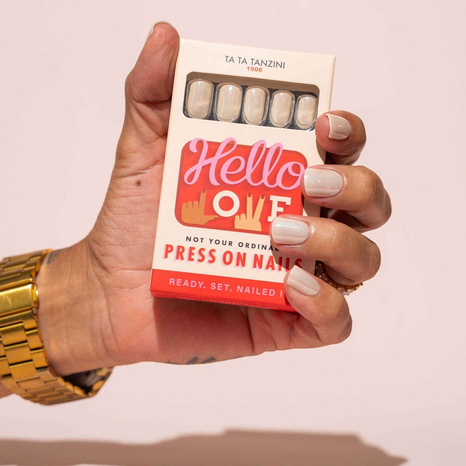 Hand holding a box of press-on nails with a colorful label against a plain background