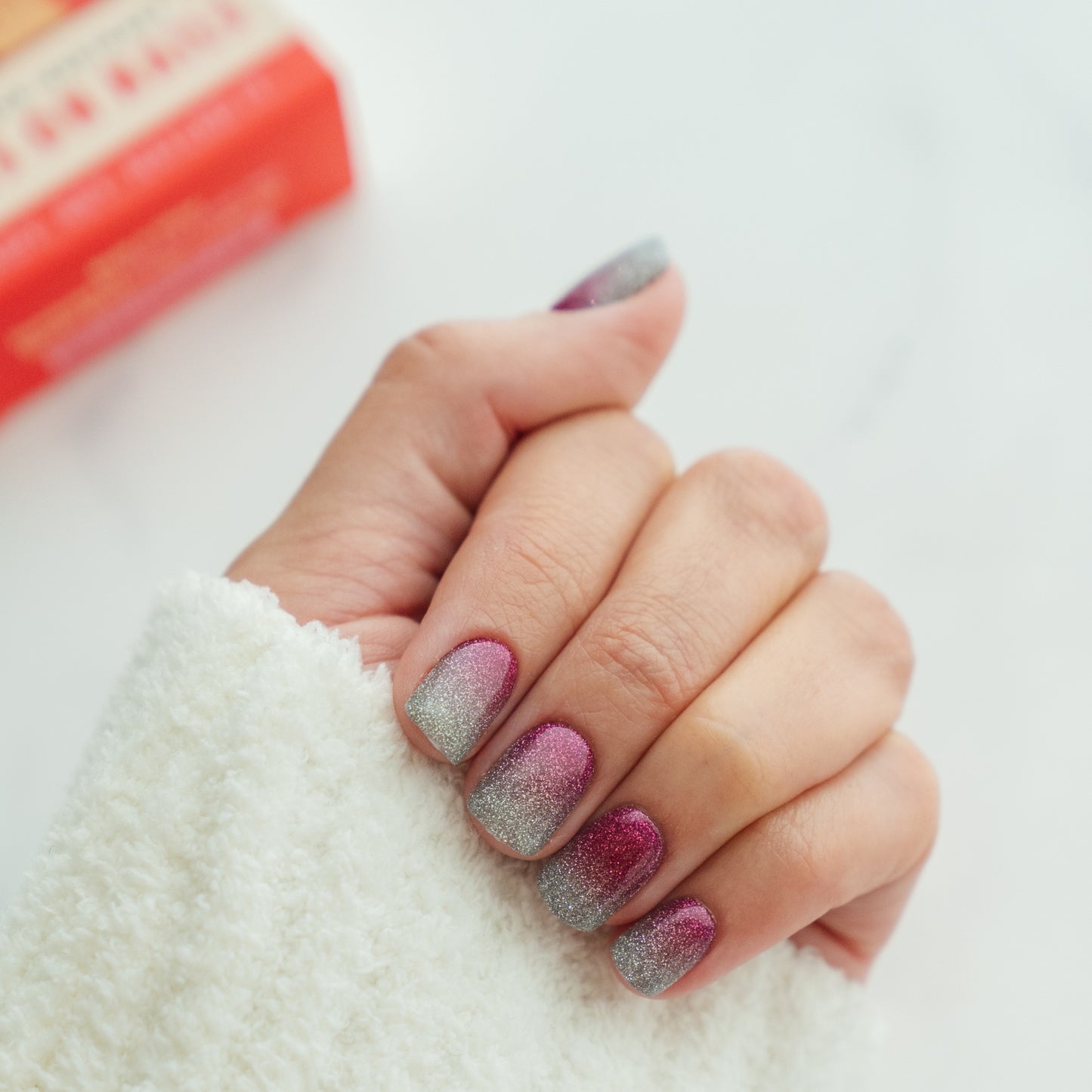 Hand with pink and silver ombre nails on a white background