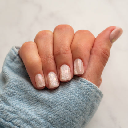 Hand with glittery press on nails wearing a light blue sleeve on a neutral background