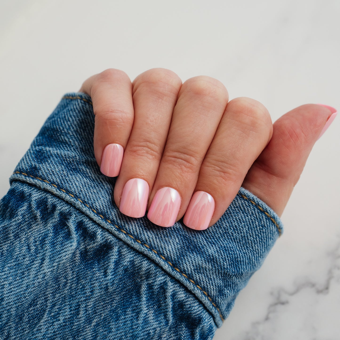 Hand with pink press on nails holding a blue denim fabric against a marble background