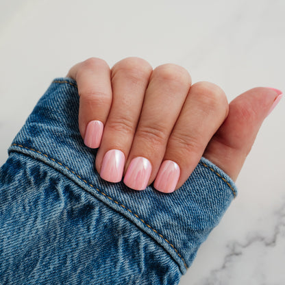 Hand with pink press on nails holding a blue denim fabric against a marble background