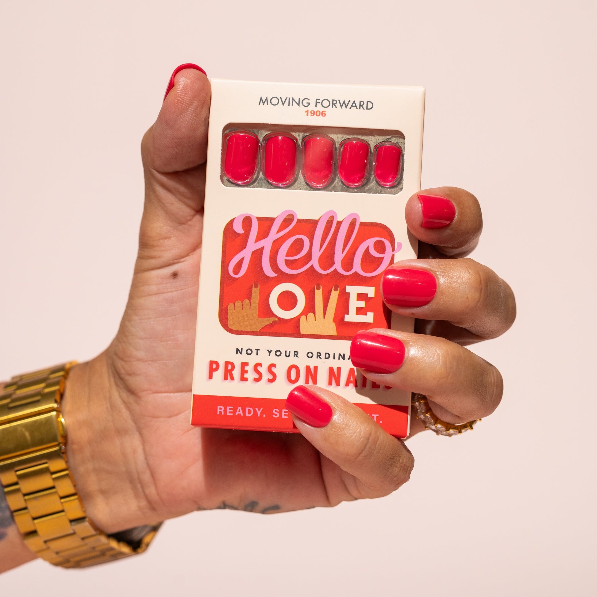Hand holding a box of press-on nails with pink red nails and 'Hello Love' branding.