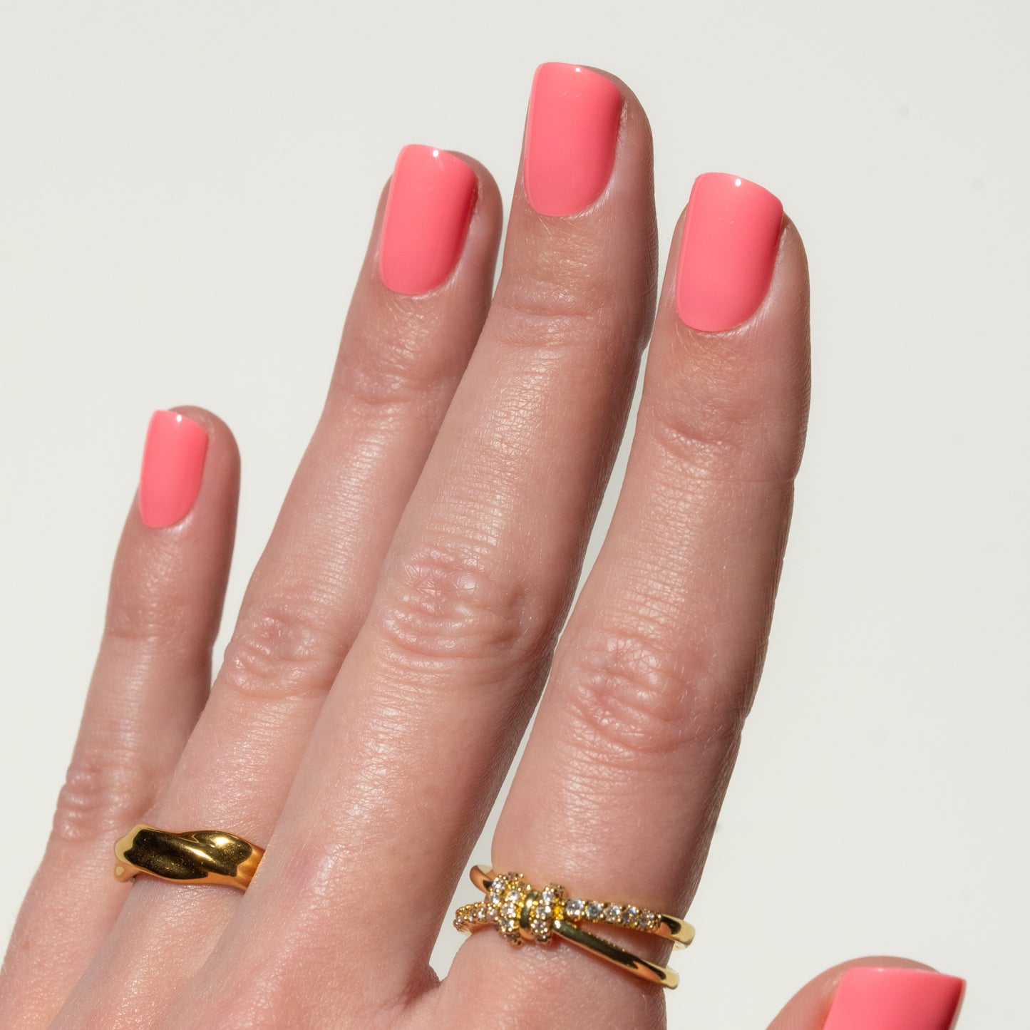 Hand with pink press on nails wearing two gold rings on a light gray background