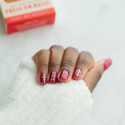 Hand with red and black plaid nail design on a white background