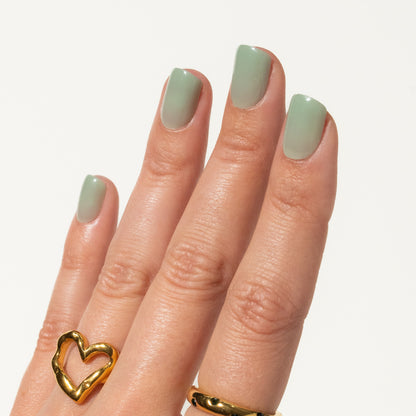Hand with green nails and a gold heart-shaped ring on a white background