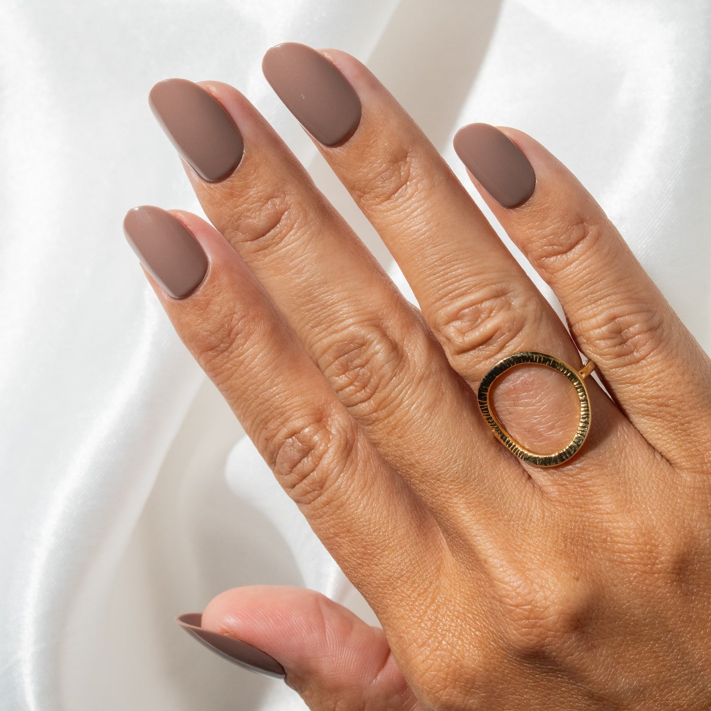 Hand with brown press on nails and a gold ring on a white background