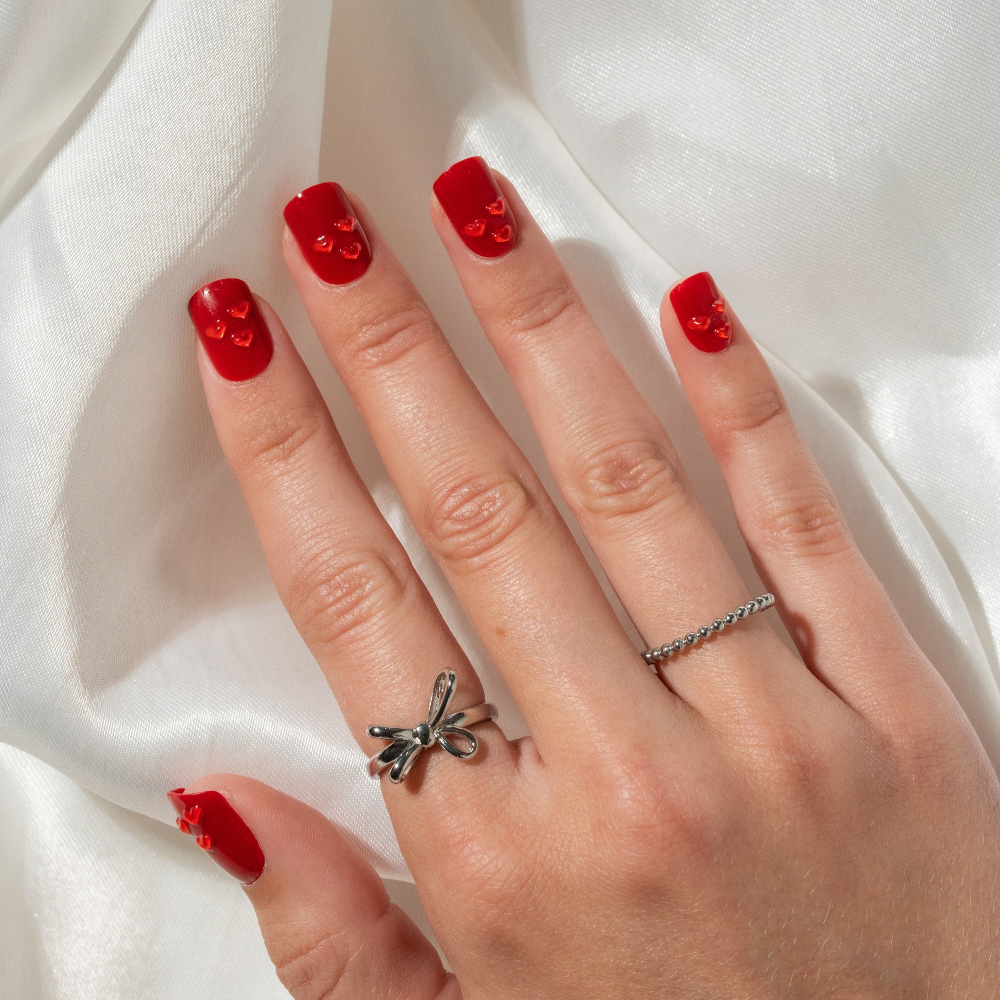 Hand with red press on nails and a silver ring on a white fabric background