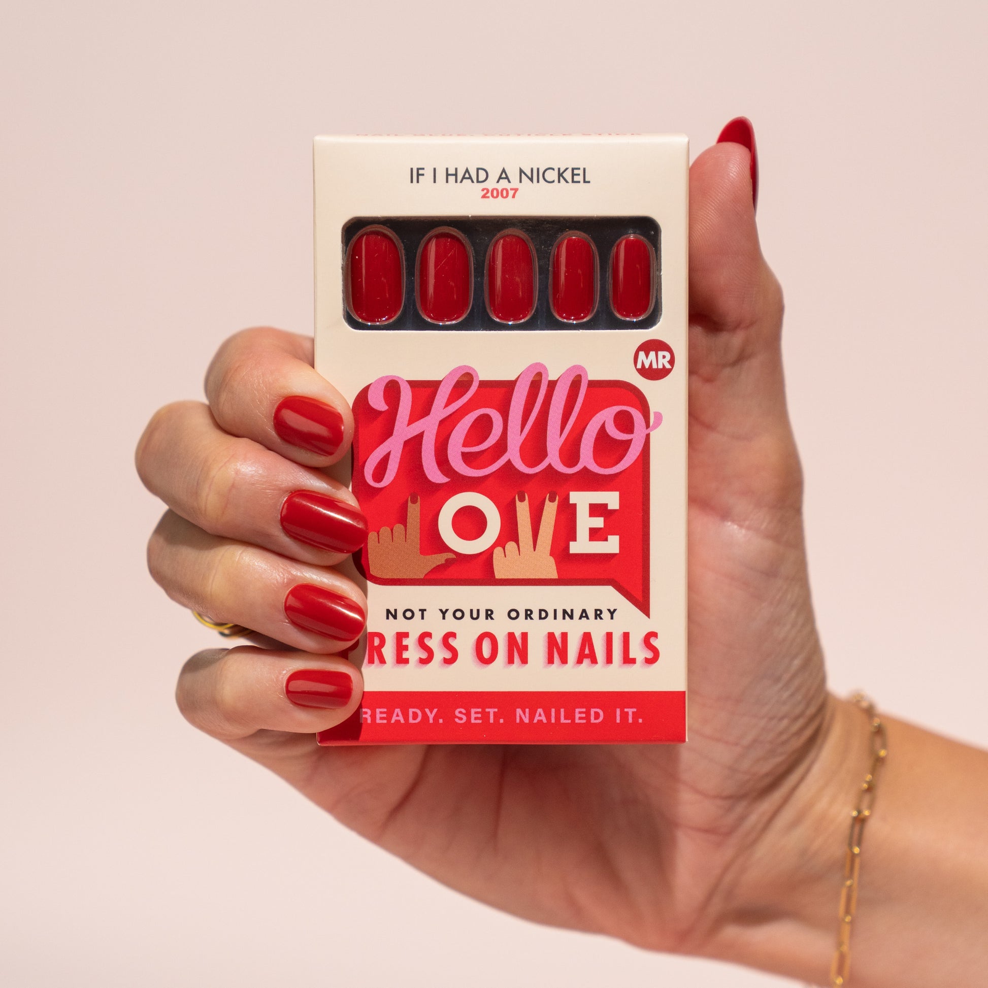 Hand holding a box of press-on nails with red nails, against a plain background