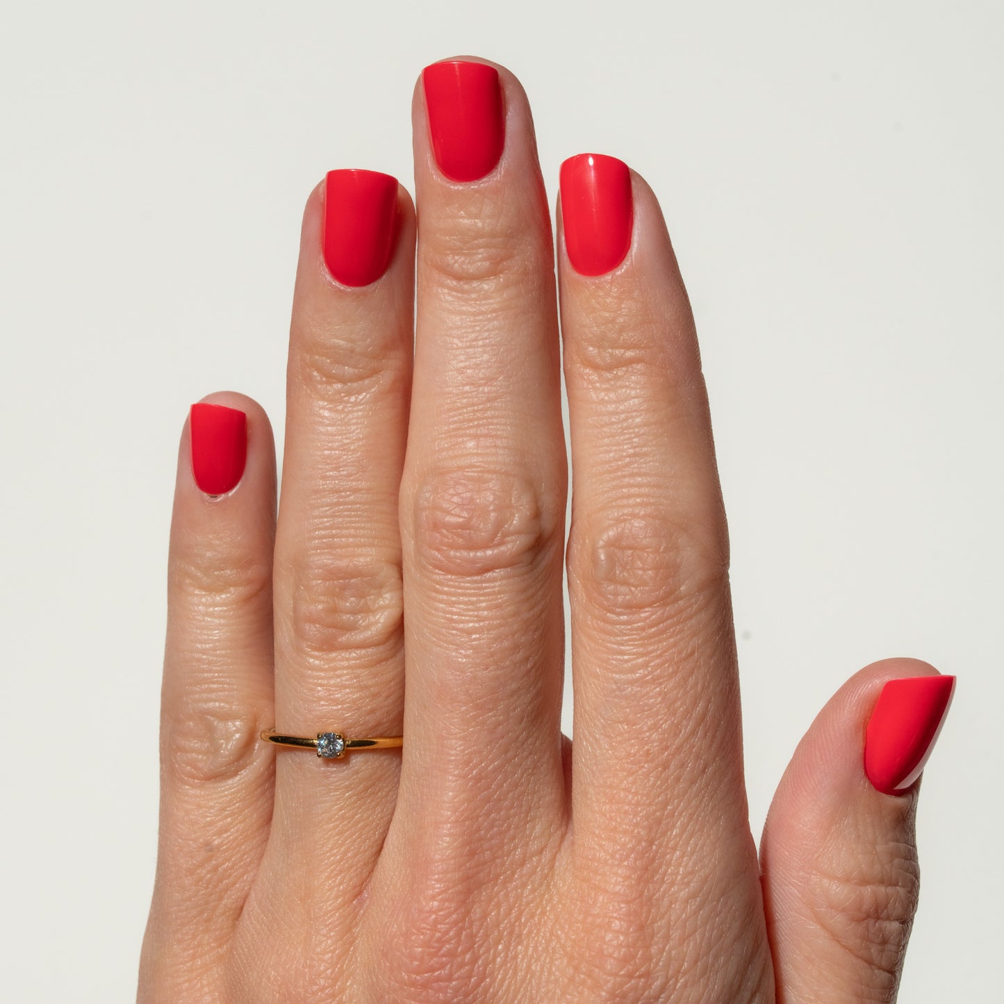 Hand with red press on nails wearing a gold ring on a light gray background