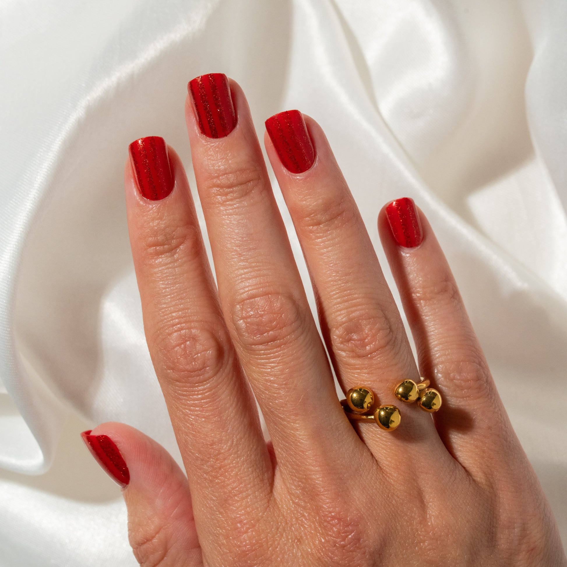 Hand with red press on nails wearing a gold ring on a white background