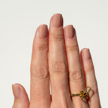 Hand wearing a gold ring with a bow design on a light background