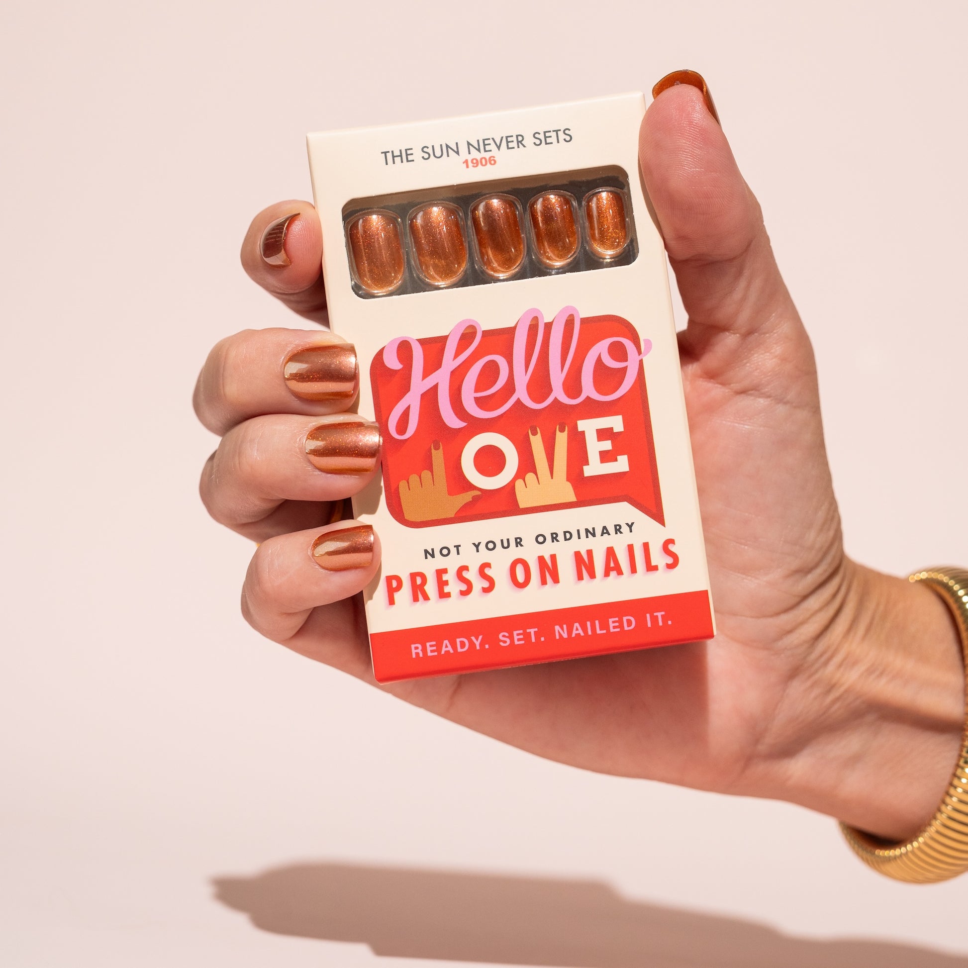 Hand holding a box of 'Hello Love' press-on nails with a light pink background